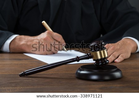 Midsection of judge writing on paper at table in courtroom