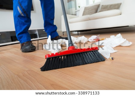 Low section of male janitor sweeping crumpled papers on floor in living room