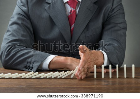 Midsection of businessman stopping dominoes falling on wooden desk