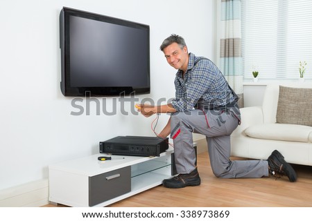 Full length of male technician installing TV set top box at home