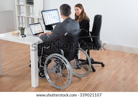 Mature Disabled Businessman And Businesswoman Working Together On Computer In Office