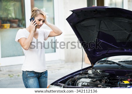 Young woman using mobile phone while looking at broken down car on street