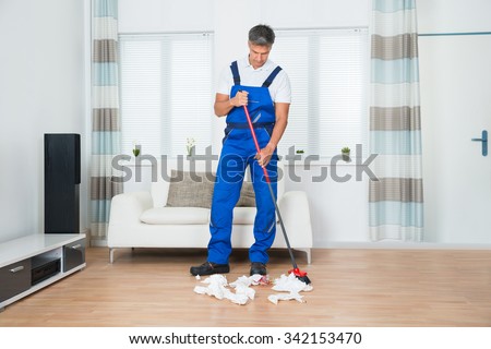 Full length of male janitor sweeping crumpled papers on floor in living room