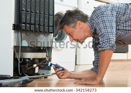 Side view of handyman checking refrigerator with flashlight at home