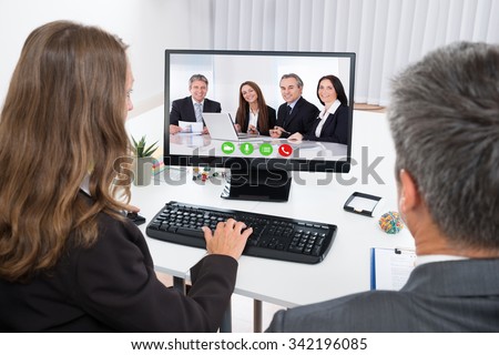Two Businesspeople Video Chatting With Colleagues On Computer In Office