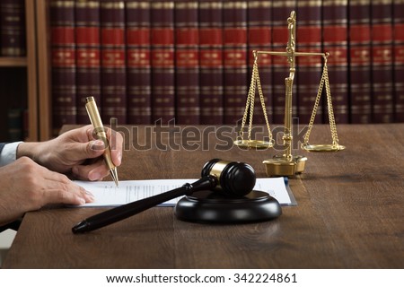 Cropped image of male judge writing on legal documents at desk in courtroom