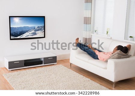 Young African Woman Lying On Sofa Watching Television