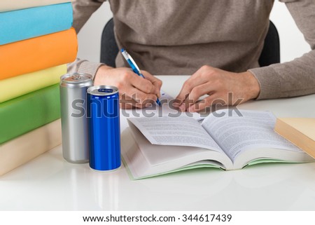 Midsection of male student writing in book while studying at table