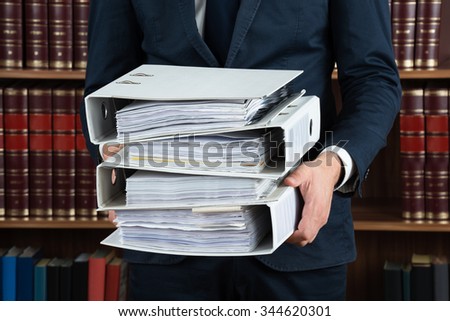 Midsection of male lawyer carrying stack of ring binders in courtroom
