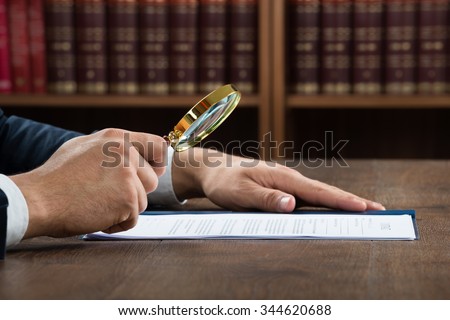 Cropped image of lawyer examining documents with magnifying glass in courtroom