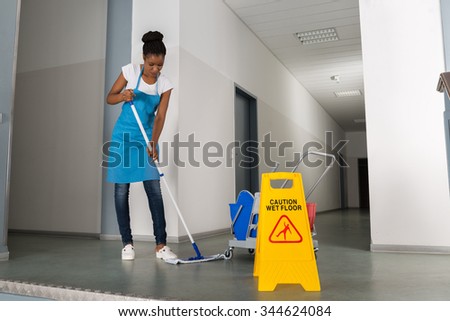 African Woman Mopping Corridor Besides Caution Sign