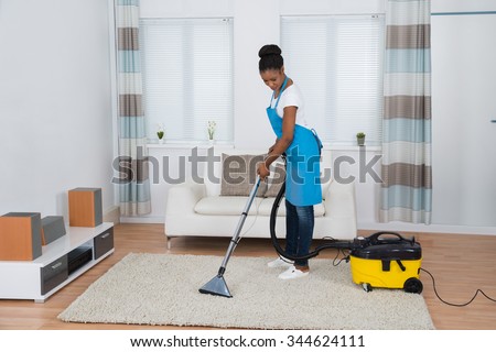 Young African Woman Cleaning Carpet With Vacuum Cleaner