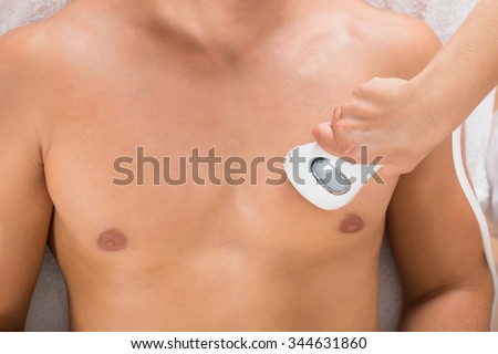 High Angle View Of A Female Beautician Giving Laser Epilation On Man\'s Chest