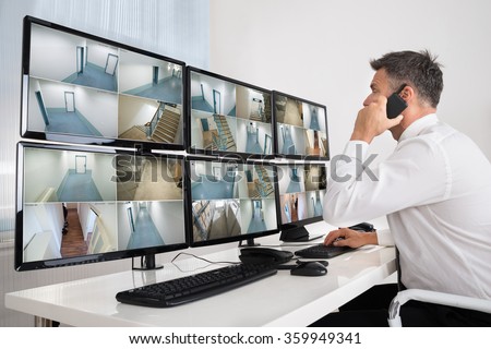 Side view of security system operator using walkie-talkie while looking at CCTV footage