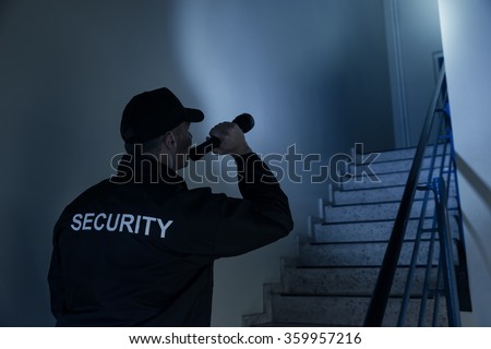 Rear view of security guard searching on stairway with flashlight in office building