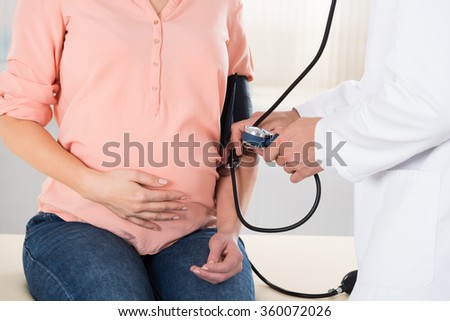 Midsection of male doctor checking pregnant woman\'s blood pressure in hospital