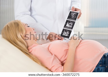 Midsection of doctor showing ultrasound scan to pregnant woman in hospital