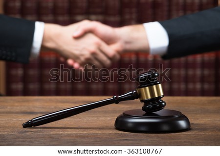 Gavel on wooden table with judge and client shaking hands in background at courtroom