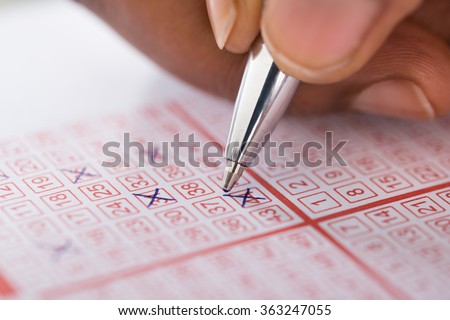 Close-up Of Person\'s Hand Marking Number On Lottery Ticket With Pen