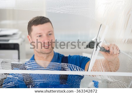 Smiling mid adult worker cleaning soap sud on glass window with squeegee