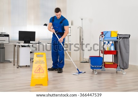 Full length of male janitor mopping floor in office