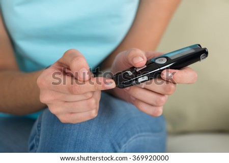 Midsection of young woman using glucometer to check blood sugar level at home