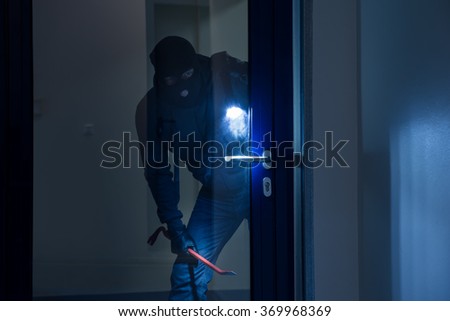 Thief with flashlight trying to break glass door with crowbar