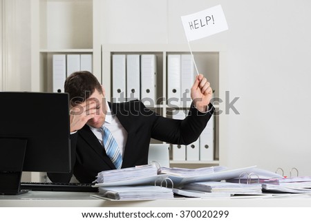 Overworked accountant holding help sign while working at desk in office