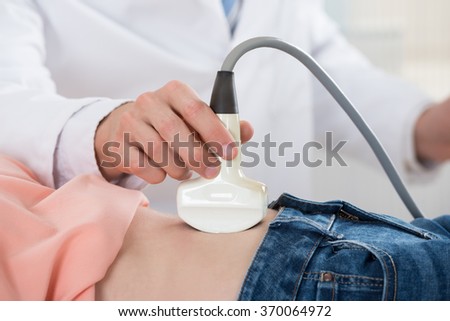 Closeup of male doctor moving ultrasound probe on pregnant woman\'s stomach in hospital