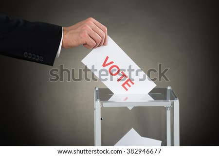 Close-up Of A Businessperson Hand Putting Vote Into Ballot Box