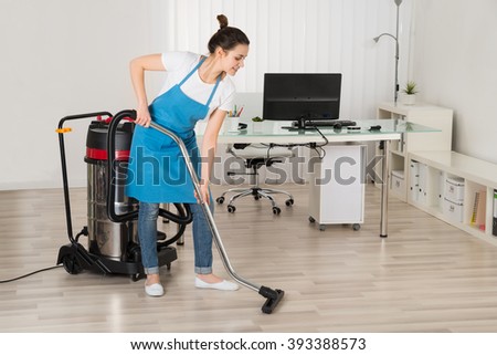 Female Janitor Cleaning Floor With Vacuum Cleaner In Office