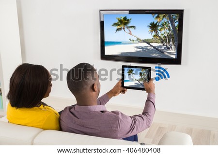 Happy Couple Sitting On Sofa Watching Television