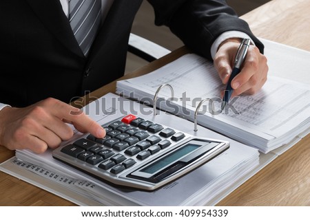 Close-up Of Male Accountant Calculating Tax At Desk In Office
