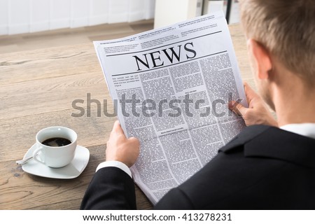 Young Businessman Reading Newspaper At Desk In Office