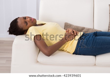 Young African Woman Lying On Sofa Suffering From Stomach Ache