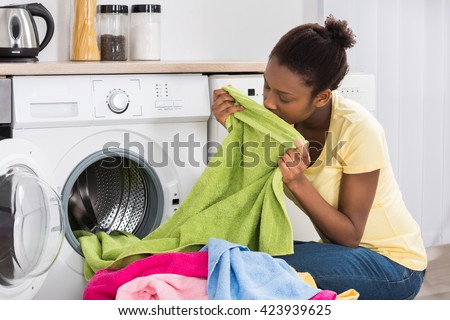 Young African Woman Smelling Clothes After Washing At Home