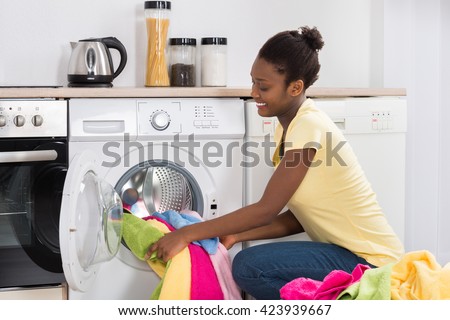 Young African Woman Putting Clothes Into Washing Machine At Home