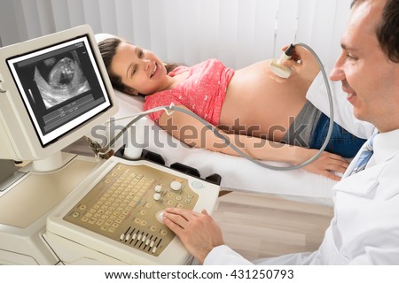 Happy Male Doctor Moving Ultrasound Transducer On Pregnant Woman\'s Belly While Looking At Screen