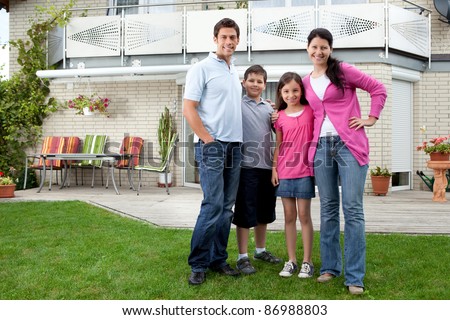Portrait of happy young family standing in front of their house