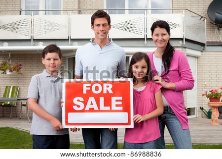 Portrait of happy family selling their home holding for sale sign board