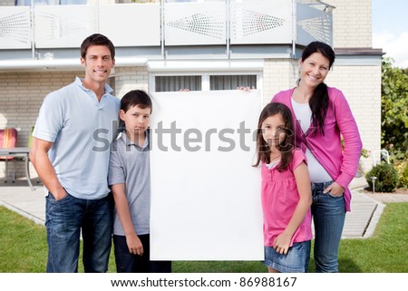 Portrait of happy young family standing outside with a blank sign board