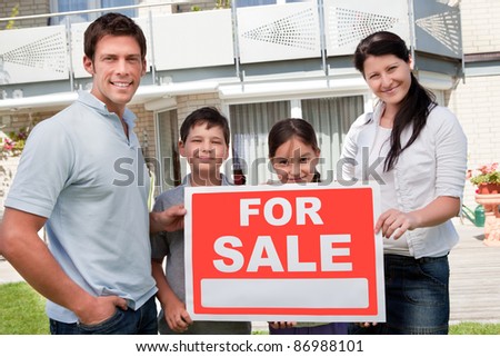 Portrait of young family selling their home holding for sale sign - Outdoors