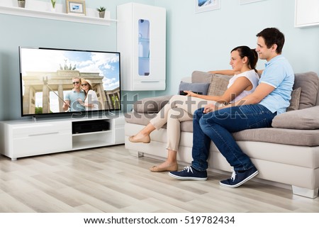 Happy Couple Watching Movie On Television Together While Sitting On Sofa At Home