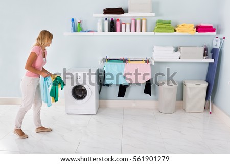 Happy Woman Walking With Stained Clothes To Washing Machine In Utility Room