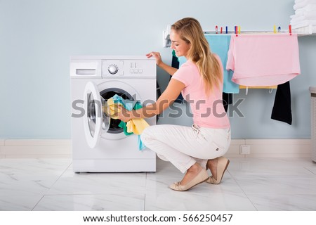 Woman Loading Dirty Clothes In Washing Machine For Washing In Utility Room