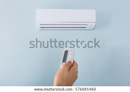 Close-up Of Young Woman Hand Operating Air Conditioner With Remote Control
