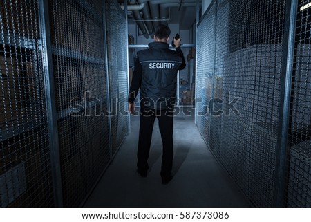 Rear View Of A Security Guard Standing In The Warehouse Holding Flashlight