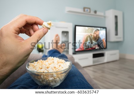 Close-up Of A Person Enjoy Watching Movie On Television While Eating Popcorn