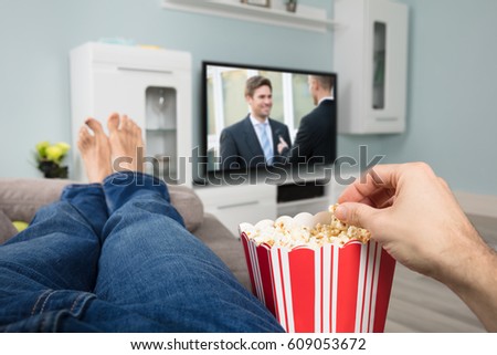 Close-up Of A Person Enjoy Watching Movie On Television While Eating Popcorn