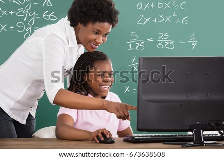 Smiling African Teacher Teaching Her Student On Computer In Class
